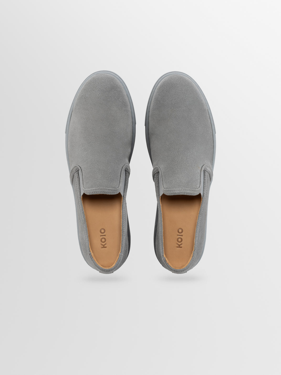 Top view of Taranto grey suede sneakers showcasing slip-on design and tan footbeds on a light grey background