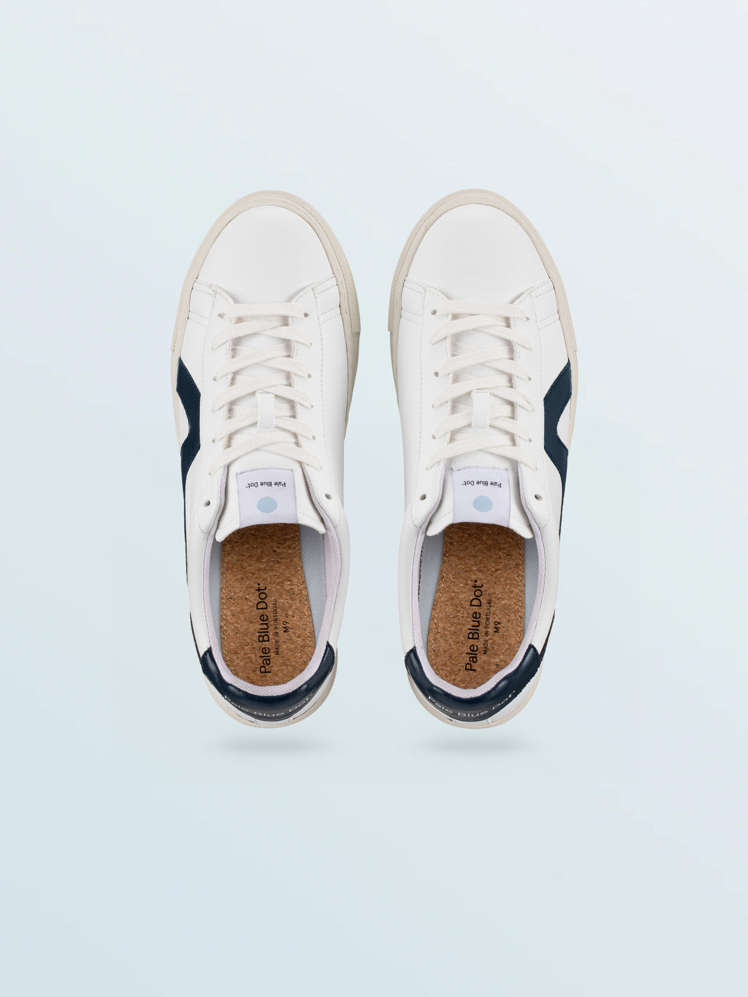 Top view of Vegan 01 sneakers in Iceberg with white uppers, navy side panels, and cork footbeds on a pale blue background