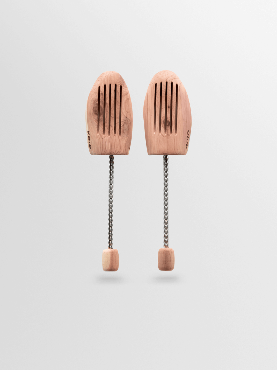Front view of a pair of KOIO shoe trees showcasing slotted wooden fronts and spring-loaded shafts with a light gray background