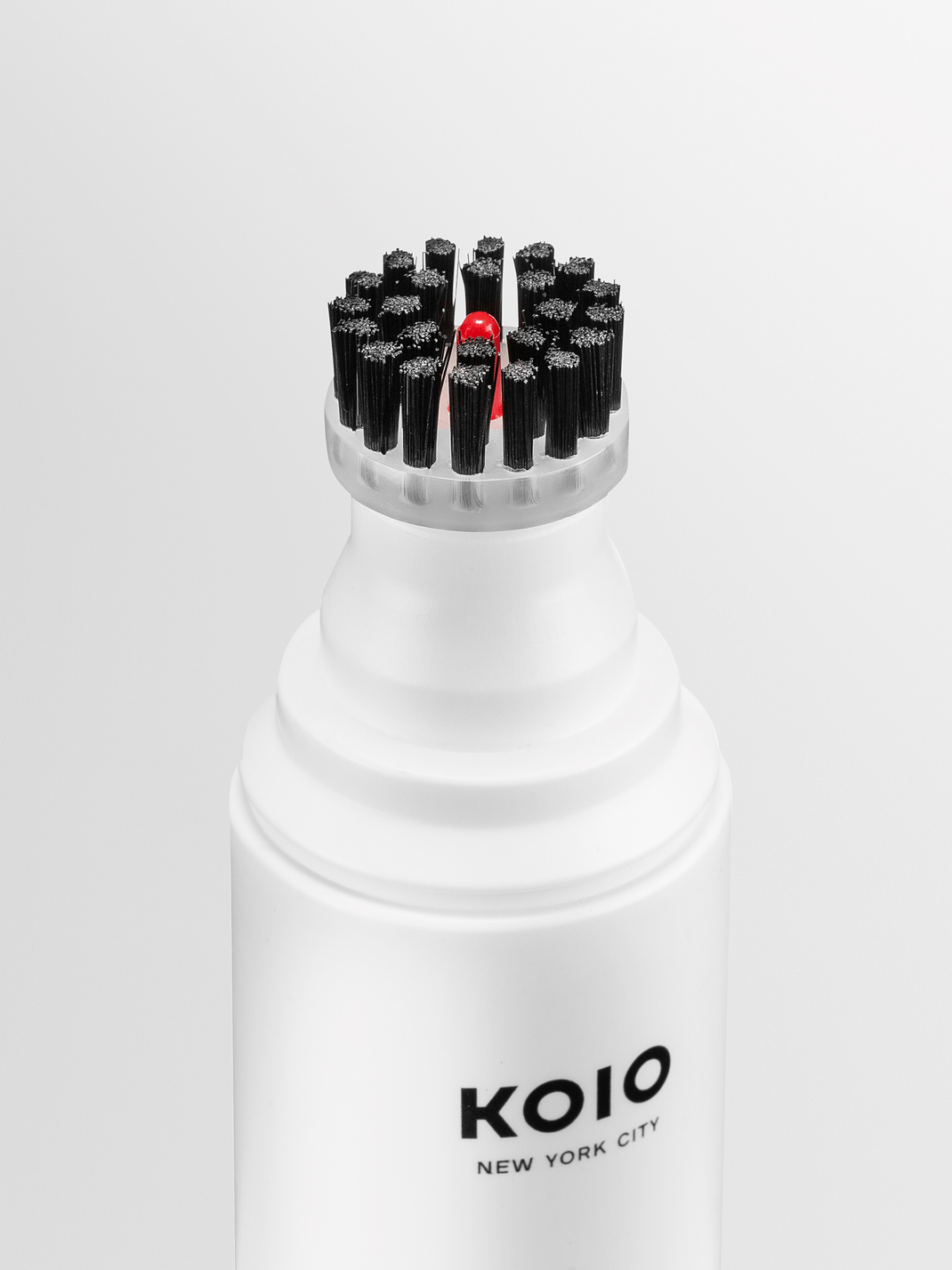 Front view of KOIO Eco Cleaner showcasing its integrated black-bristle brush with a white bottle against a light background