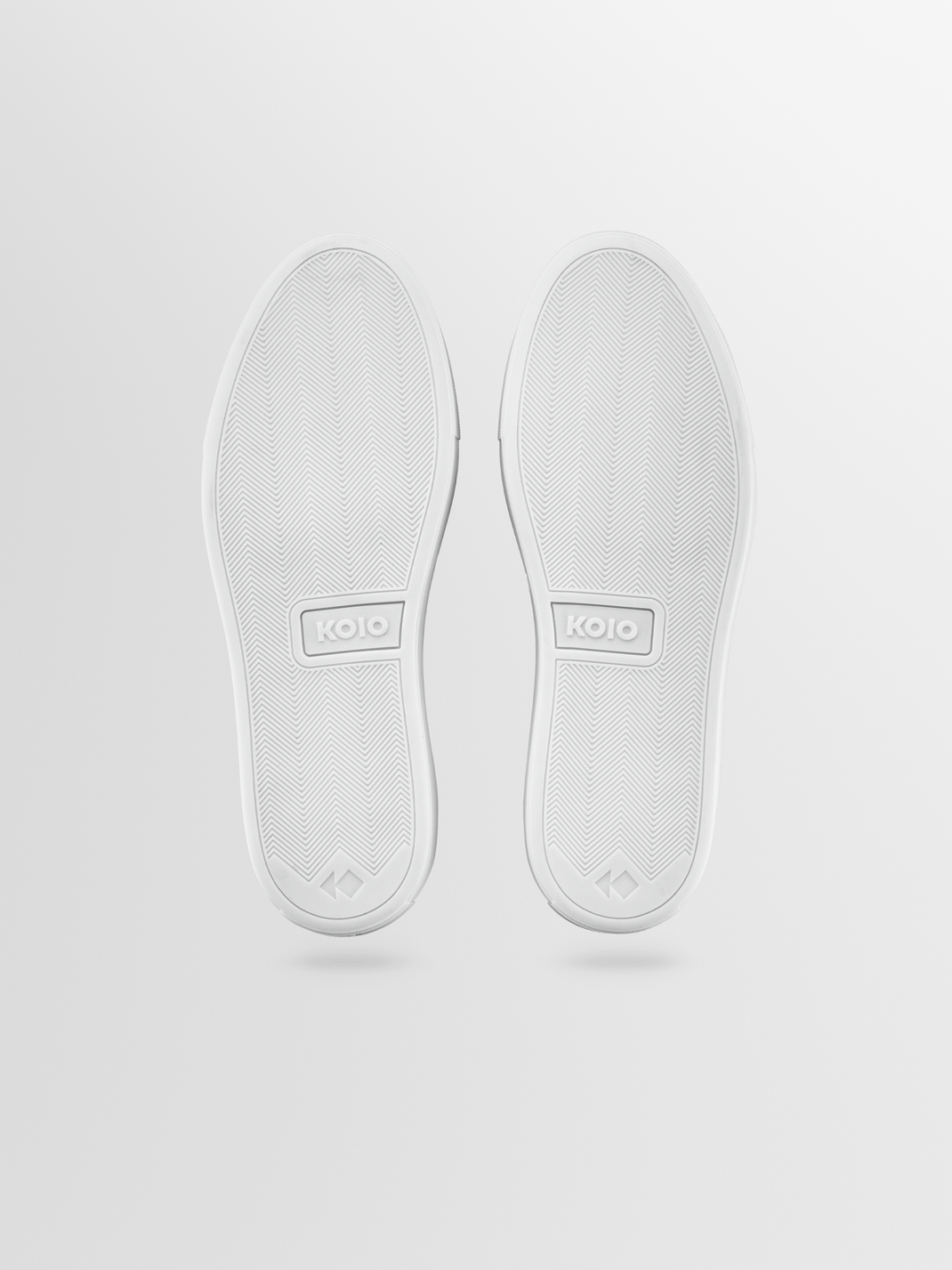 Bottom view of Portofino suede sneakers in Mineral showcasing herringbone outsoles and KOIO logos on a light gray background